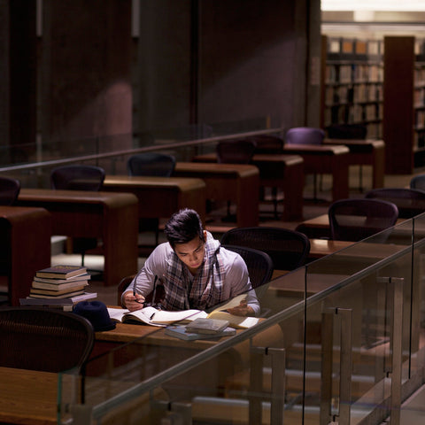 Person studying in a library with bookshelves and tables in the background