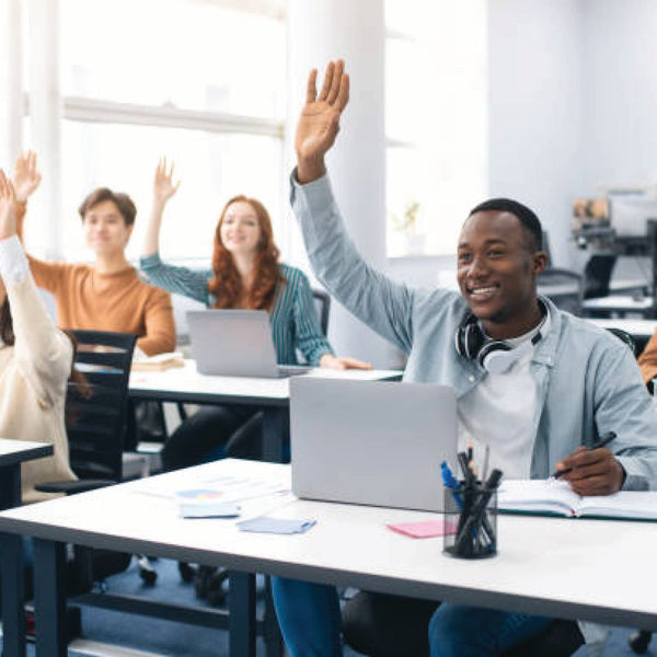 Diverse college students raising their hands enthusiastically in a bright classroom.