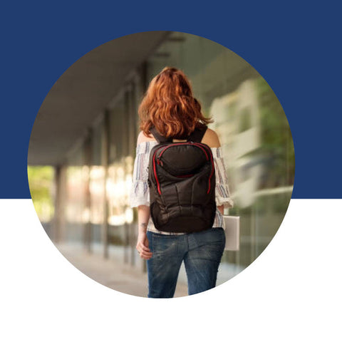 A woman seen from behind, walking down a hallway with a backpack on.