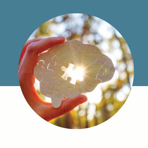 Hand holding a brain-shaped light bulb against a natural background