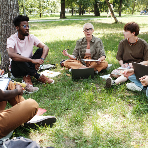 Group of people sitting on grass in a park, using laptops and tablets.