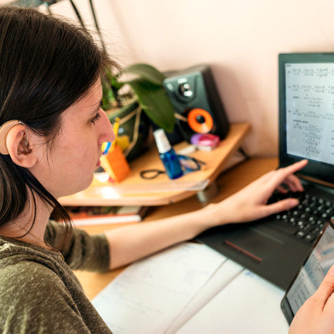 Student using a laptop and smartphone with a hearing aid, representing accessible technology and inclusive digital learning.