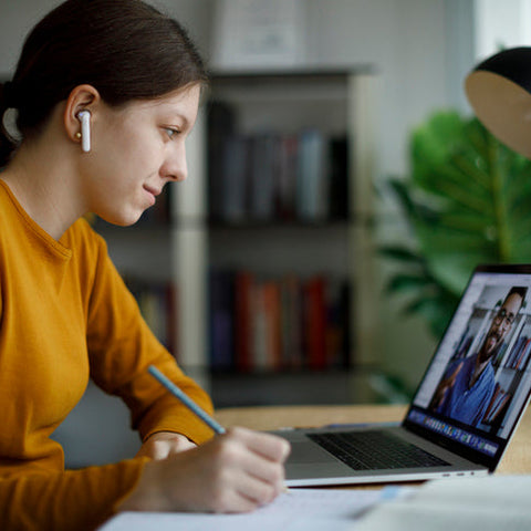 Woman sitting at a desk with a laptop, pen, and notebook in a home office setting.