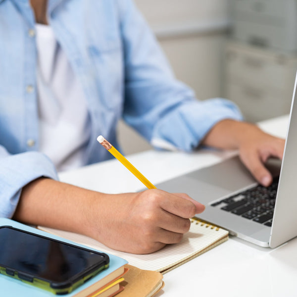Person working at a desk with a laptop, smartphone, and notebook.