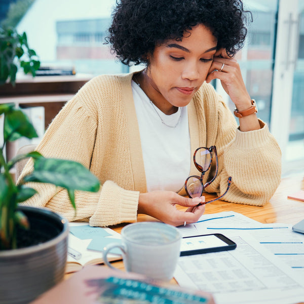 Woman sitting at a desk with a laptop, phone, and documents, looking stressed.