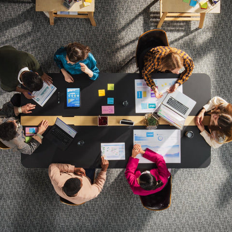 Group of people working together at a table with laptops and papers in a modern office setting.