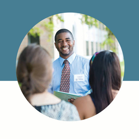 Man in a blue shirt and tie interacting with two women outdoors, with a blue and white background.