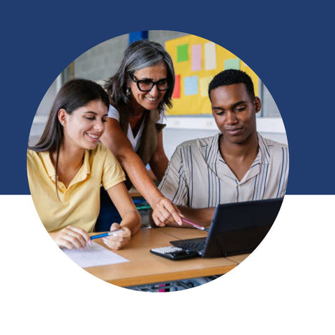 A teacher leaning in to help two students working together at a laptop in a classroom.