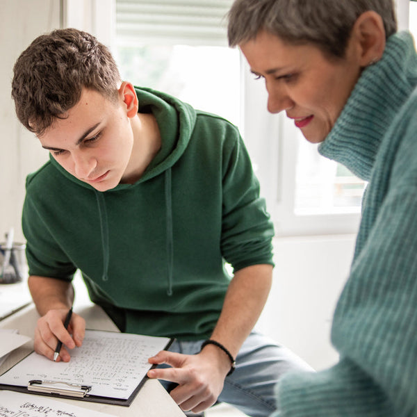 Woman and young man working together on a project at a desk with a laptop and papers.