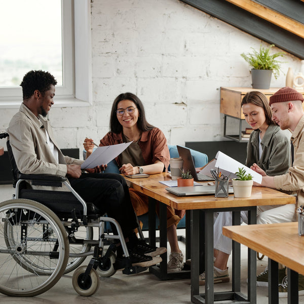 Person using a wheelchair sitting at a table with colleagues in an office setting.