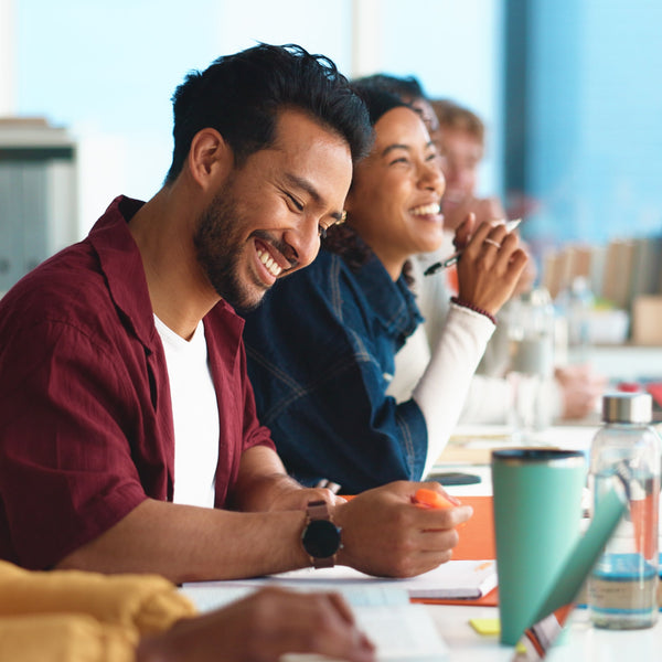 Group of people sitting around a table in a modern office setting, smiling and engaged in conversation.