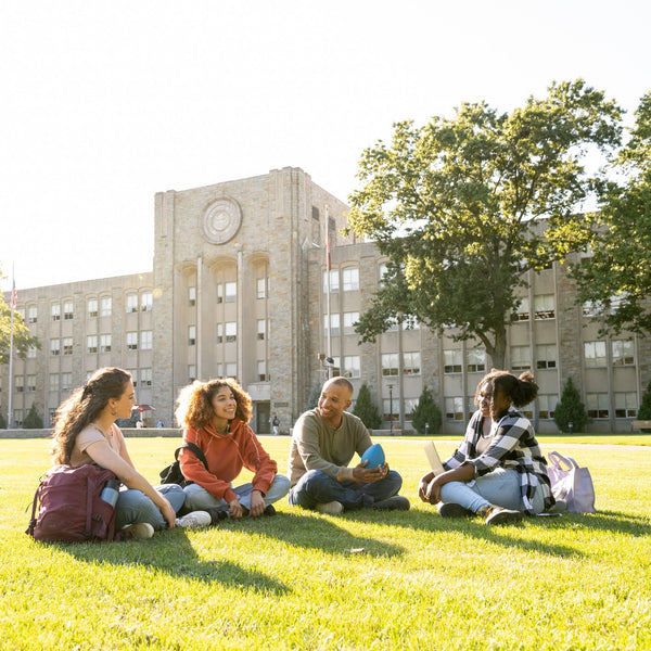 Four students sitting on a grassy area in front of a school building.