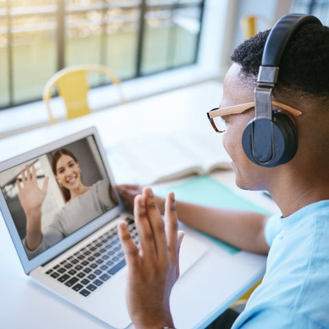Person wearing headphones and interacting with a laptop screen showing another person.