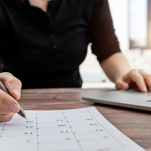Person using a pen on a calendar with a laptop in the background