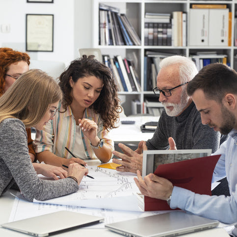 Team of professionals collaborating around a table, reviewing documents and discussing plans, representing teamwork, strategy, and capacity-building in the workplace.