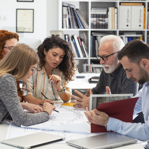 Team of professionals collaborating around a table, reviewing documents and discussing plans, representing teamwork, strategy, and capacity-building in the workplace.