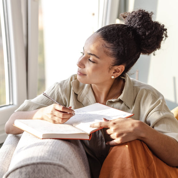 Woman sitting by a window, writing in a notebook.