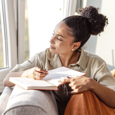 Woman sitting by a window, writing in a notebook.