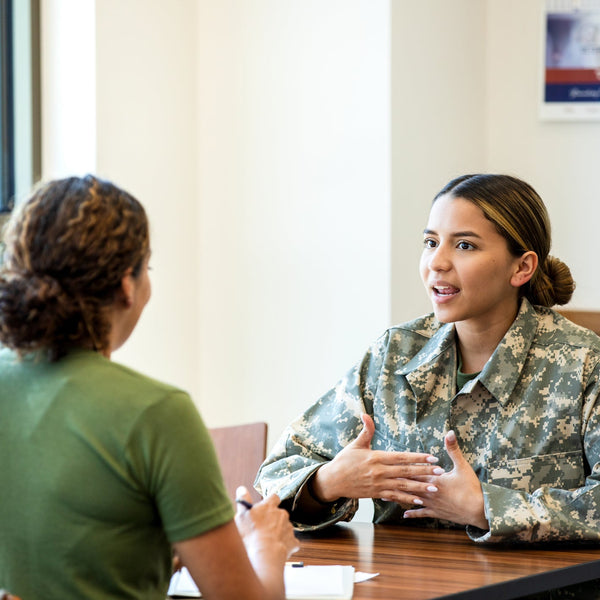 Young woman in military uniform speaking with a counselor or advisor in an office setting.