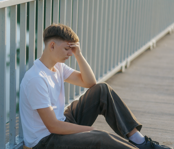 Young man  sitting along a fence looking distressed