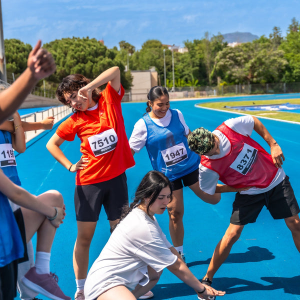 Group of people participating in a race or physical activity on a blue track with trees in the background.