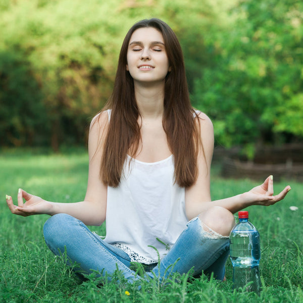 Woman meditating on grass with a water bottle nearby