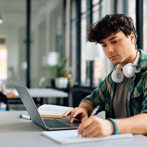 Person working on a laptop with headphones around their neck in an indoor setting.