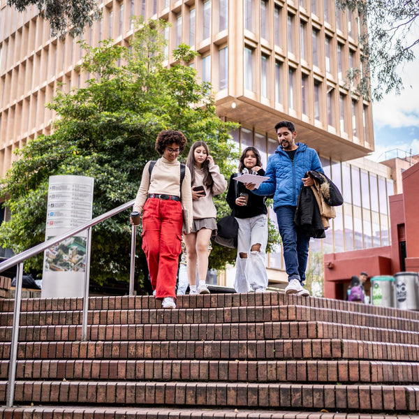 Group of students walking up a set of stairs in front of a modern building with trees and a clear sky.