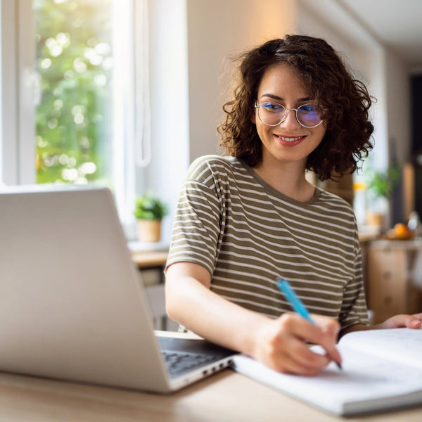 Woman sitting at a desk with a laptop and notebook, smiling.