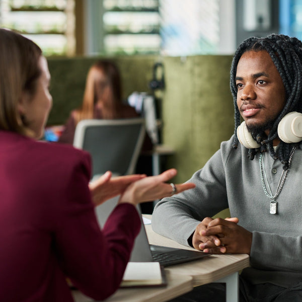 Two people engaged in a conversation at a desk in an office setting.