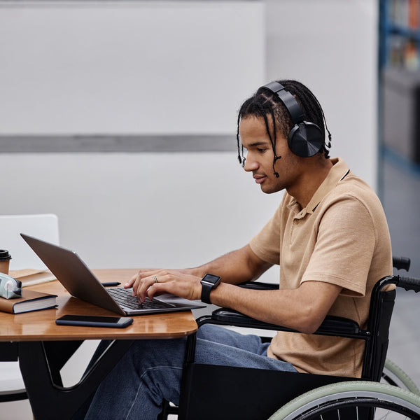 Man in a wheelchair using a laptop with headphones in an office setting