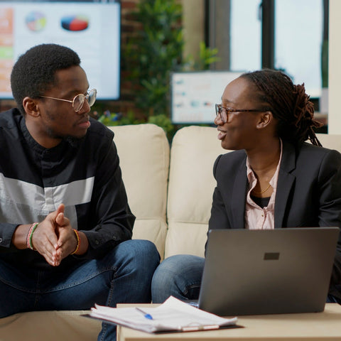 Two people sitting on a couch with a laptop and papers, discussing something.