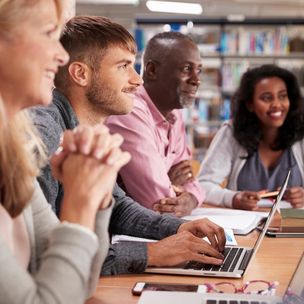 Group of people sitting around a table in a library setting, using laptops.