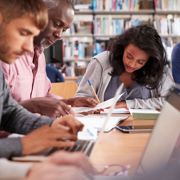Group of people studying together in a library with books and laptops.