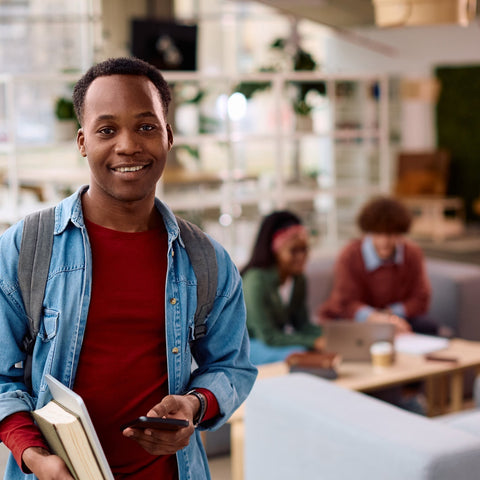 Man holding books in a modern office or library setting with people in the background