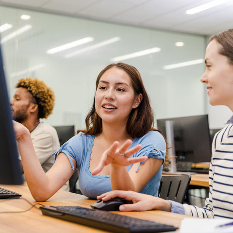 Two women and a man working together at a computer in an office setting.